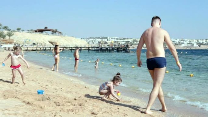 父亲带着孩子在红海的沙滩上玩沙子。