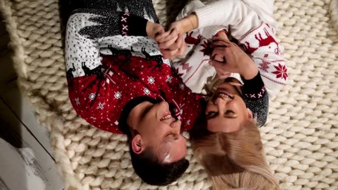 一对恋爱中的圣诞毛衣夫妇躺在针织毯子上的地板上。