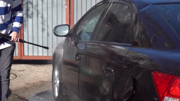 一名男子用高压水射流冲洗汽车上的污垢。洗车专用洗涤剂。在房子前面洗一辆车。