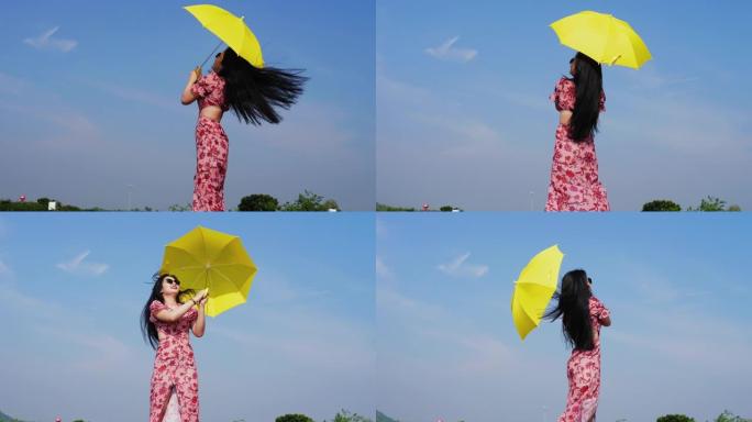 戴着墨镜的快乐亚洲女人在蓝天下撑着黄色的伞。