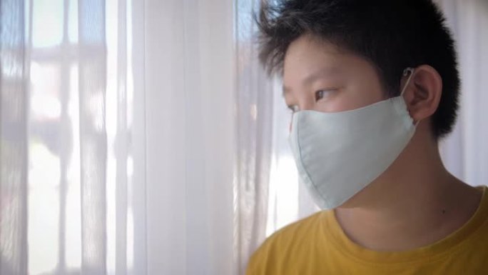 亚洲生病的年轻青春期男孩戴着口罩站在家里的窗户附近，检疫概念。