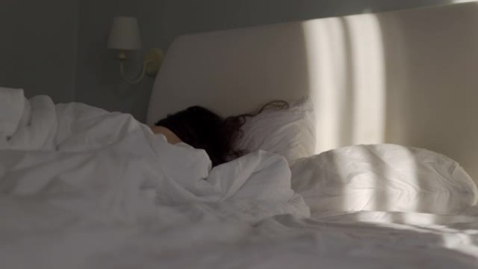 女人睡在床上，棕色长发放在枕头上，阳光放在床上。