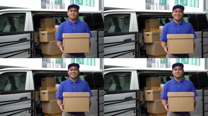 电晕病毒概念，笑脸蓝色送货英俊的亚洲男子拿着包裹纸板箱站在货车前。4k分辨率和慢动作拍摄。