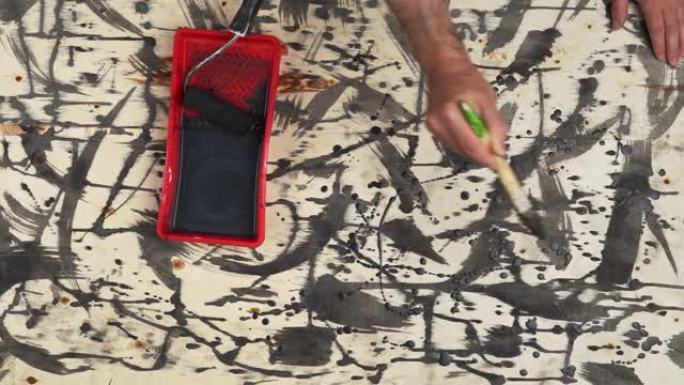 抽象画黑色在木质背景上，死在垃圾风格上，深色画在胶合板上，男人的手用刷子或滚筒