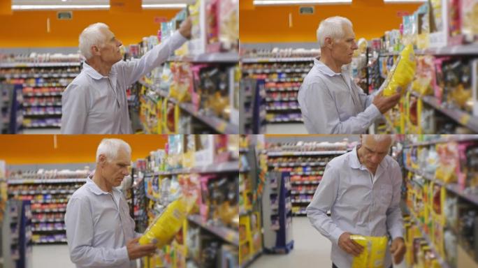 超市里的高级男人。穿着蓝色衬衫的白发老人选择零食，并将食物篮放在商店货架背景上。