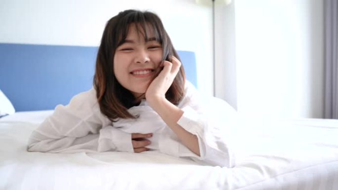 美丽的亚洲女人在床上微笑快乐她躺在卧室的毯子下舒适舒适地在酒店房间休息人们早上健康的生活方式