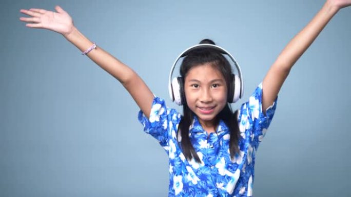 快乐的亚洲女孩在粉色背景上使用耳机。