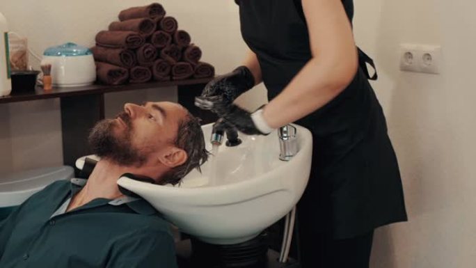 发型师在理发店用洗发水洗男性头发。理发师在切割前洗手男性头部。理发店沙龙的男性头发护理。