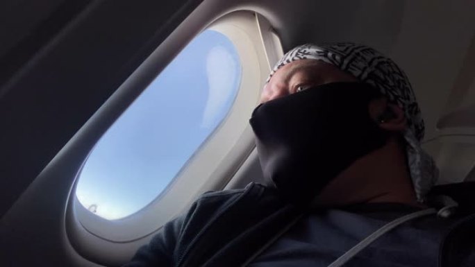 戴着医用口罩的乘客看着飞机窗外新型冠状病毒肺炎空中旅行