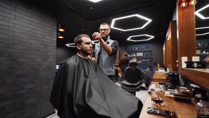 时髦的理发师在理发店用理发剪胡子的男人的头发。沙龙中的男士发型和理发。用修剪器梳理头发。理发师在复古