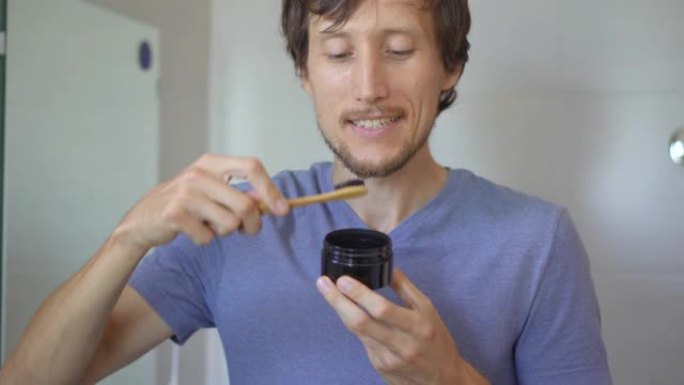 一个年轻人用竹木制成的刷子刷牙，用木炭美白牙齿。零浪费概念。可生物降解产品概念