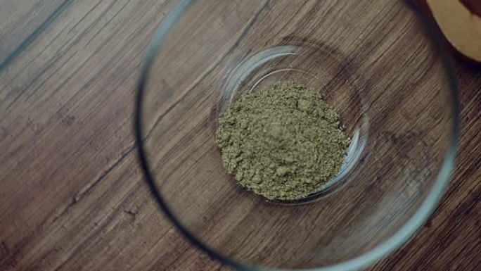在棕色木桌上的透明玻璃碗中测量1汤匙黑胡椒粉。旋转摄像机捕捉食物成分。