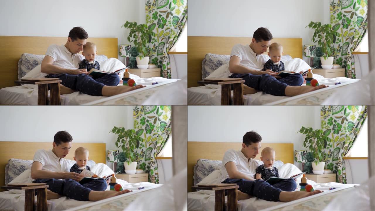 一个年轻的父亲和他的宝贝儿子坐在家里的床上读一本儿童读物