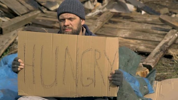 废墟附近的一个无家可归的人，上面有一个饥饿的标志，在疫情期间帮助贫困和饥饿的人