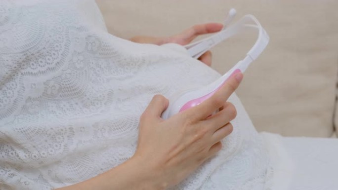 孕妇将耳机戴在肚子上，让婴儿听音乐