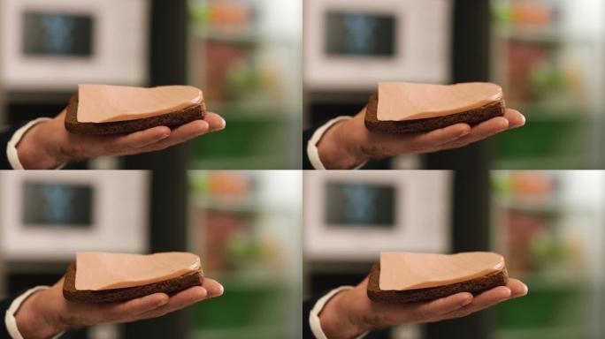 男人的手拿着一块Borodino黑麦面包的特写镜头，上面放着一片医生的香肠。库存镜头。美味香肠三明治