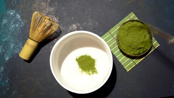 将抹茶粉放在白碗中，竹子放在蓝色的混凝土板上。