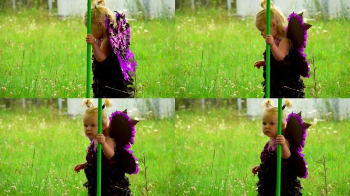 紫色蝴蝶翅膀的可爱的金发小女孩走到户外