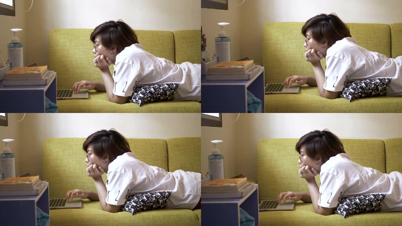 一名亚洲妇女在沙发上使用笔记本电脑。
