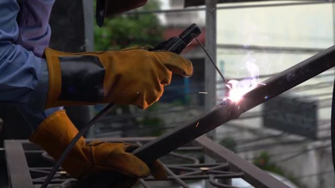 焊工通过电焊焊接钢材，并使用钢制面罩和皮手套保护自己。