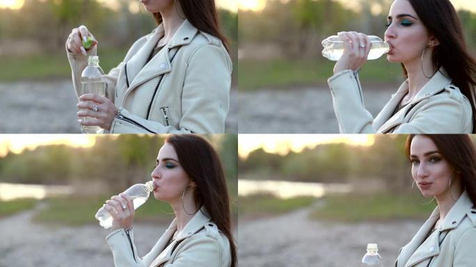 年轻女子在日落时喝水。女孩从瓶子里喝水