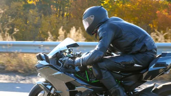 戴着头盔的男子在高速公路上骑着摩托车，背景是太阳耀斑。摩托车手在秋天的乡村路上驾驶摩托车。慢动作侧视