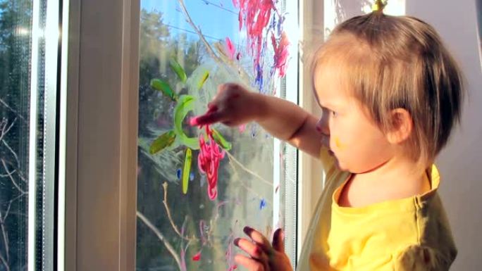 蹒跚学步的女孩正在窗户上画画，唱歌。孩子在家的概念。检疫