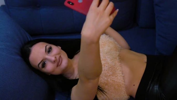 一位美丽的年轻女子在旅馆的床上用手机摄像头自拍