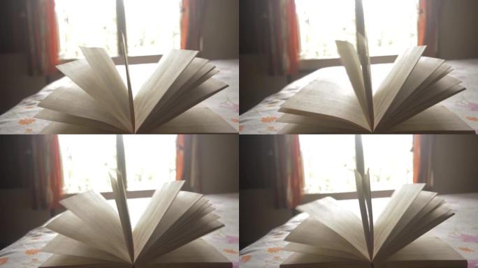 一本书在风中飘扬。打开带有页面移动背景的精装书。页面上模糊文本的出现是自然运动模糊。由窗户灯照亮。未