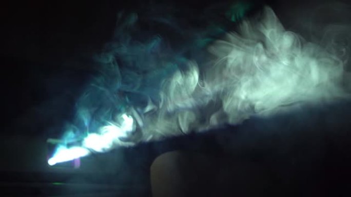 现代视频投影仪和深色背景上的彩色烟雾。烟雾在投影仪的光线中扩散