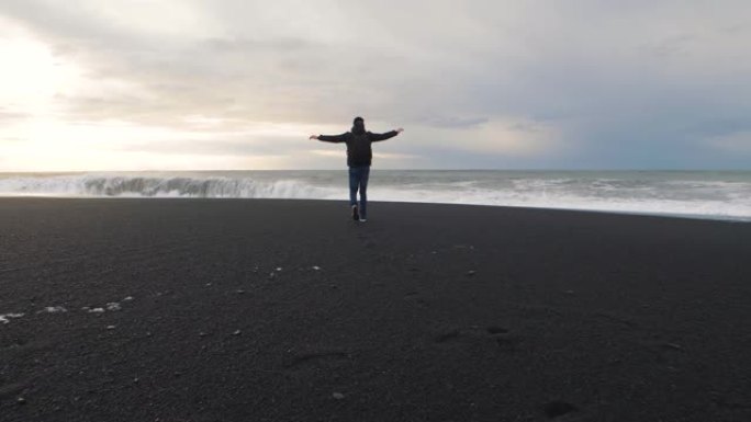 男子旅行者在冰岛火山黑沙滩上行走。慢动作镜头。雷尼斯法拉海滩