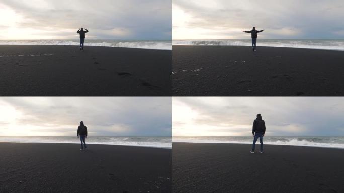男子旅行者在冰岛火山黑沙滩上行走。慢动作镜头。雷尼斯法拉海滩