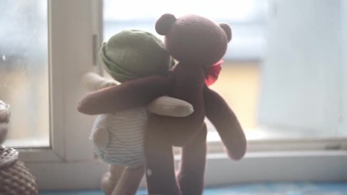 两只玩具熊站在敞开的窗前的窗台上拥抱