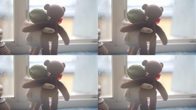 两只玩具熊站在敞开的窗前的窗台上拥抱