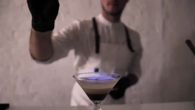 调酒师在点燃的爱尔兰奶油鸡尾酒上撒肉桂粉，产生美丽的起泡效果