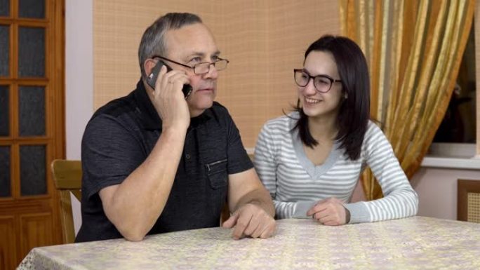 女儿教父亲如何使用电话。一名年轻女子向她的老父亲展示了在哪里点击智能手机。那个人打了电话。一家人坐在