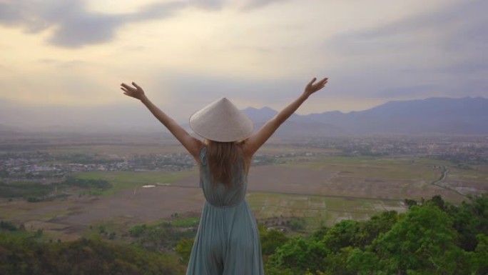 一位年轻的游客站在山顶上，可以欣赏山谷的壮丽景色。她戴着一顶亚洲帽子