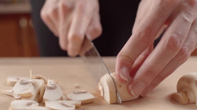用手指上漂亮修指甲的女性手用菜刀在木制砧板上切蘑菇，特写镜头。钱皮农。女人在家做饭