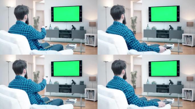 留着胡子的男人坐在客厅的沙发上，在绿屏上看电视切换频道改变音量
