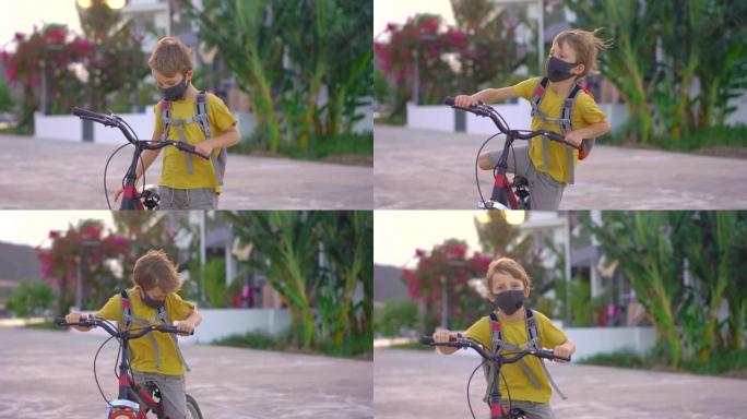 在阳光明媚的日子里，戴着医用面具的活跃学校男孩带着背包骑自行车。快乐的孩子在去学校的路上骑自行车。由