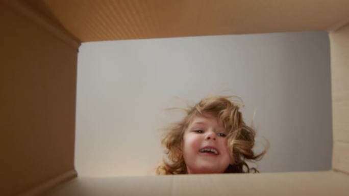 小美女在纸箱里看。内部视图。女孩笑着躲起来。