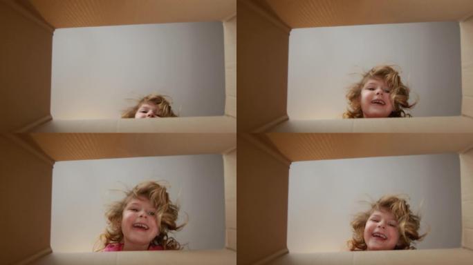 小美女在纸箱里看。内部视图。女孩笑着躲起来。
