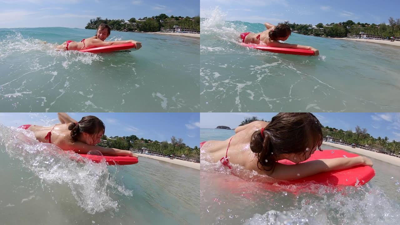 年轻女子冲浪者在热带海洋中有乐趣，并在红色冲浪板上冲浪小浪