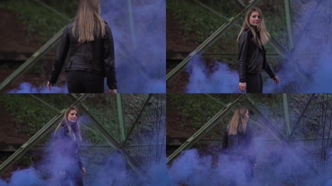 一位穿着皮夹克的漂亮年轻女子穿过一缕蓝色的烟雾走开了