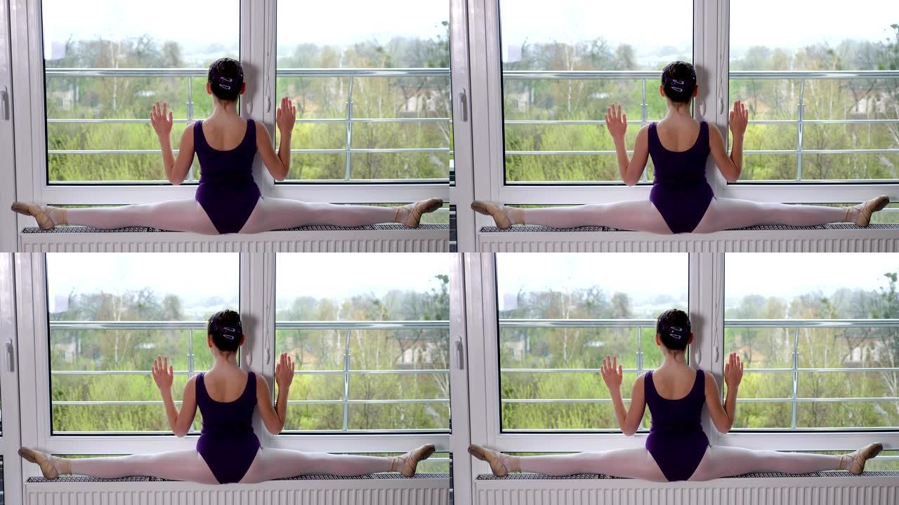 年轻的芭蕾舞演员，十几岁的女孩表演练习麻绳，伸展双腿，坐在麻绳上，在一个大全景窗户的背景下