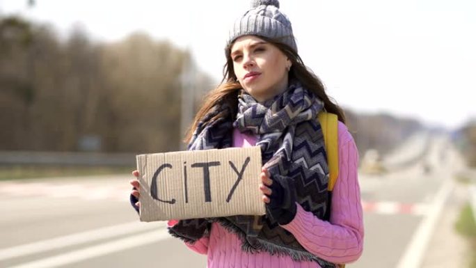 年轻严肃的女人搭便车试着用海报去城市。旅行者团队