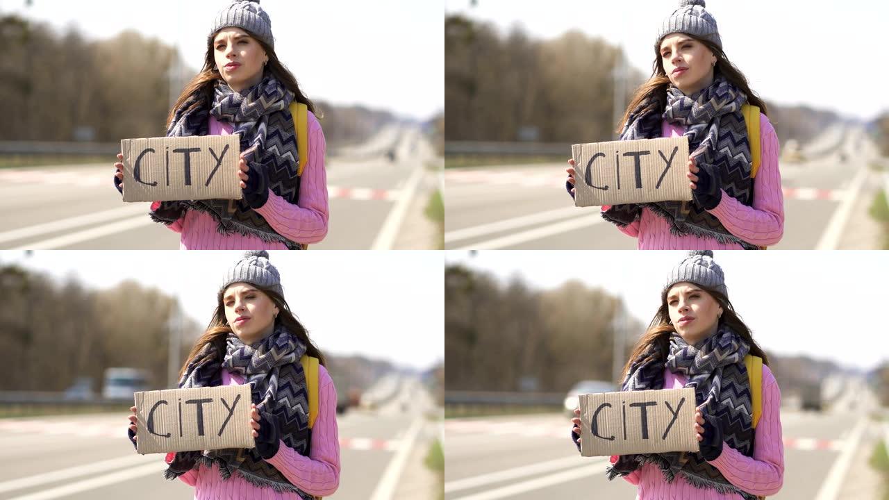年轻严肃的女人搭便车试着用海报去城市。旅行者团队
