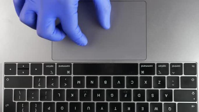 医生的手在办公室笔记本电脑上使用触控板触摸板戴蓝色手术手套