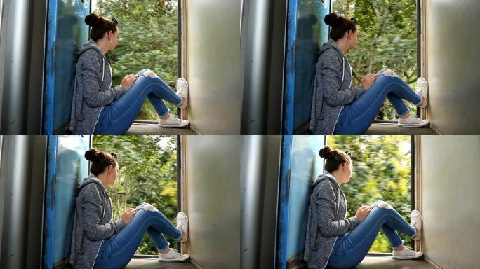年轻女子坐在行驶中的火车敞开的门附近，看着美丽的大自然。女游客乘坐铁路客运，享受夏季旅行。假期或假期