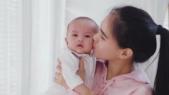 亚洲美丽的母亲温暖拥抱怀里的小女孩轻轻地抱着，然后在家卧室亲吻小孩。柔软的触摸，爱心的照顾，在家庭关